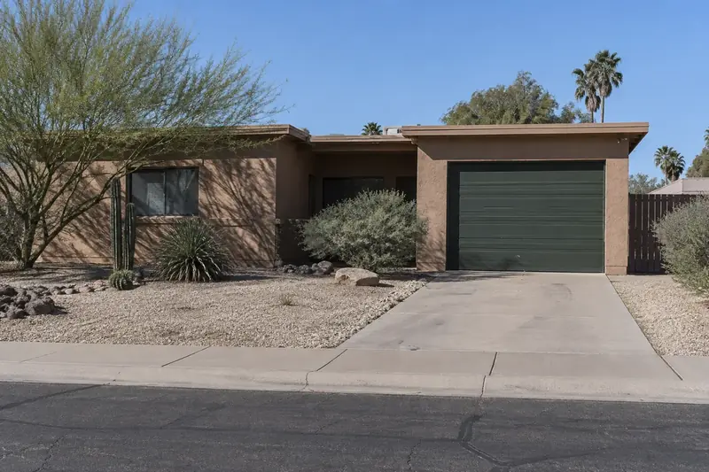 Older single-story Phoenix home with a dark green single-car garage door and a gravel yard